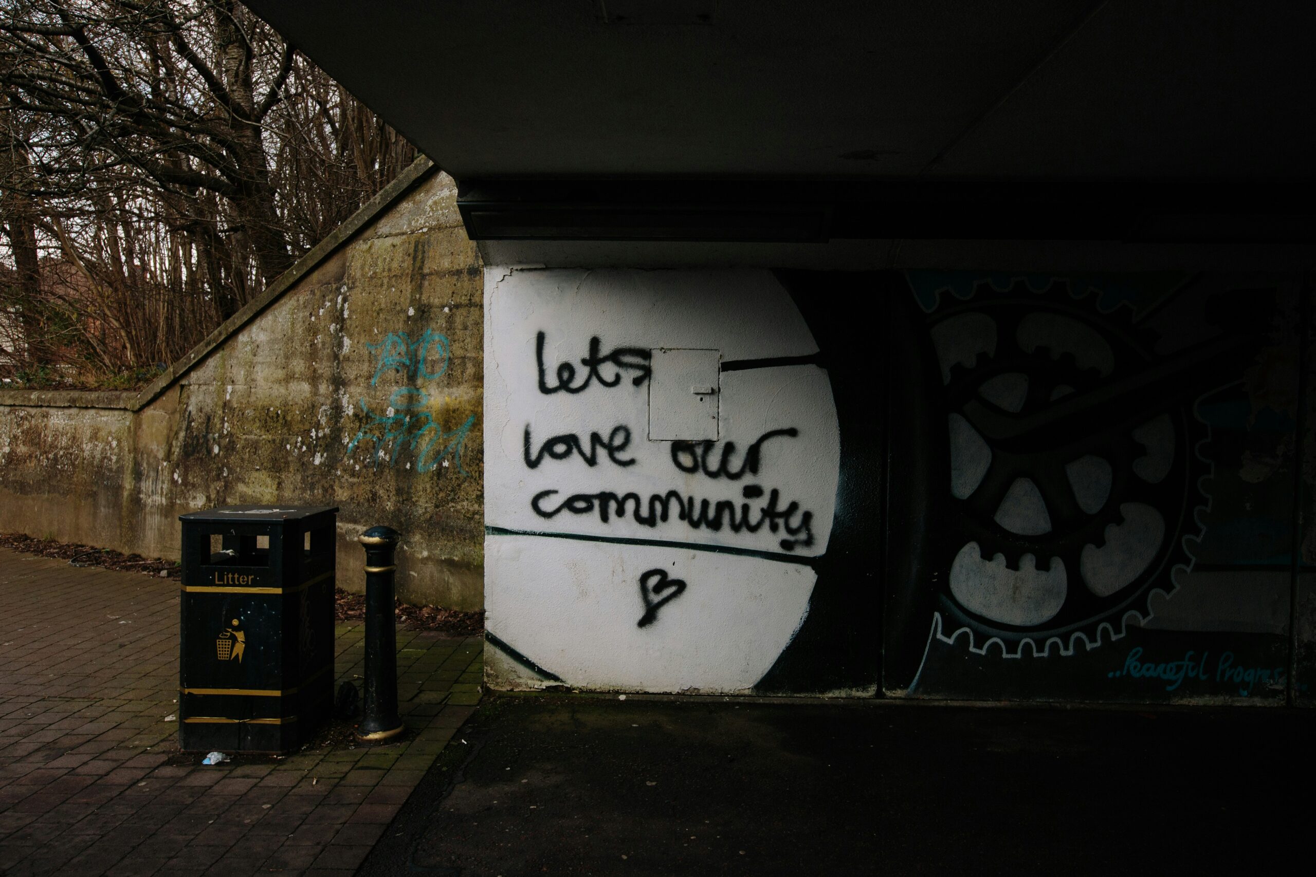 A dark road underpass has the message 'let's love our community' spray painted onto the wall