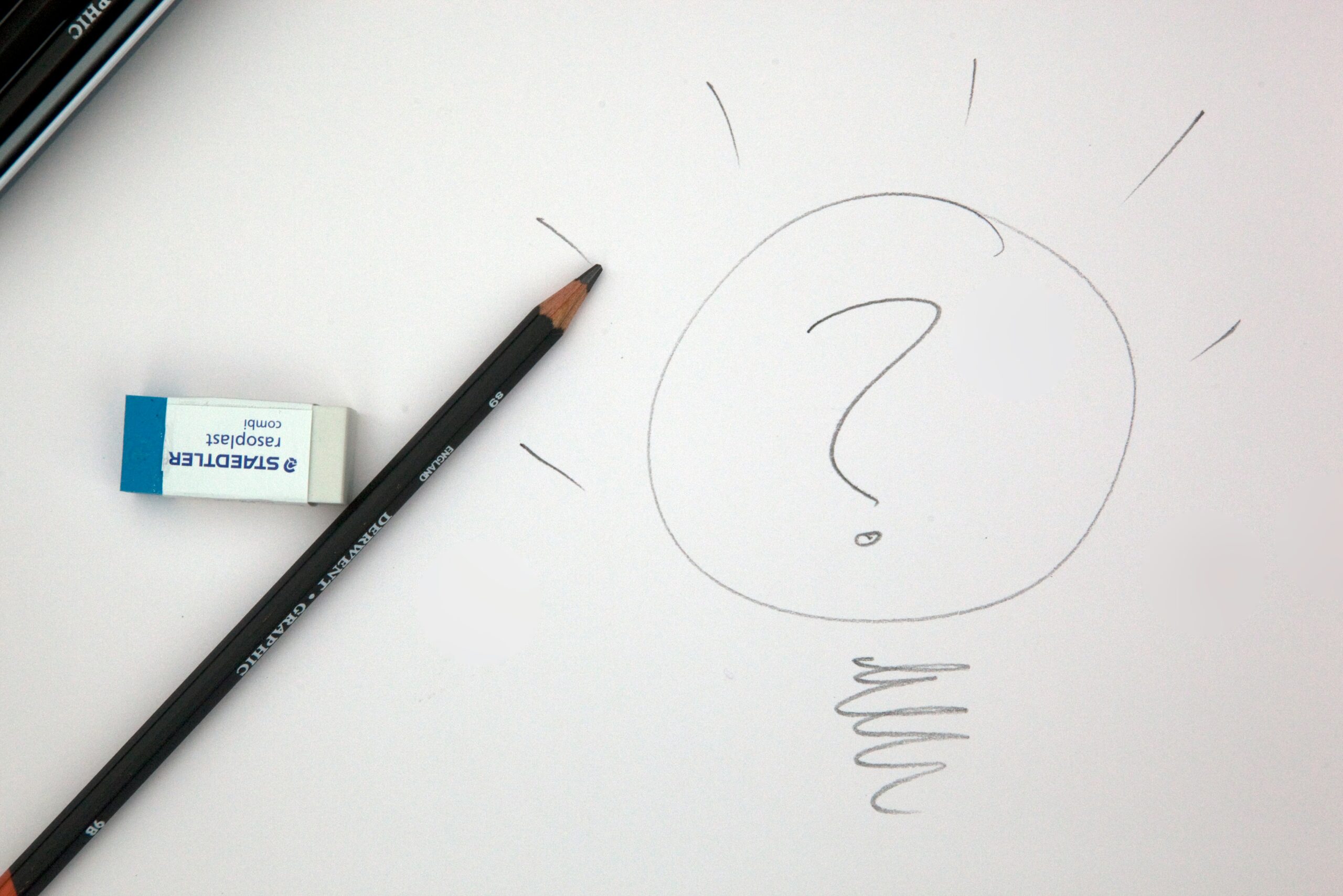 A question mark in a light bulb is drawn on a piece of white paper.